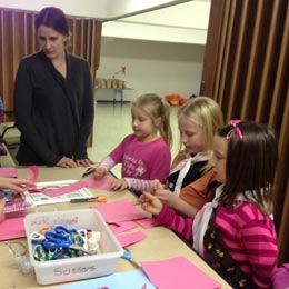 Three girls making paper crafts at a table with adult supervision.