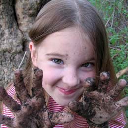 A smiling young girl with muddy hands.
