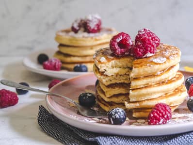 Two stacks of pancakes topped with raspberries and blueberries. 