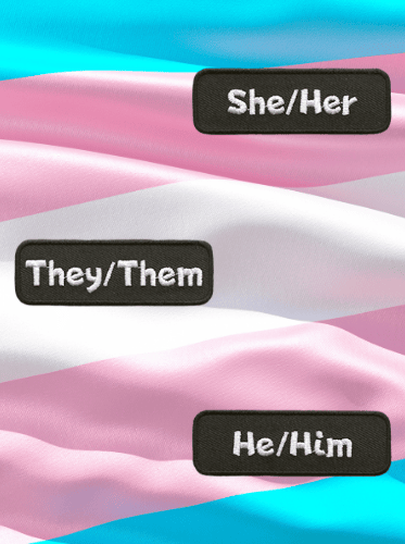 Three pronoun patches sit on top of a transgender flag.